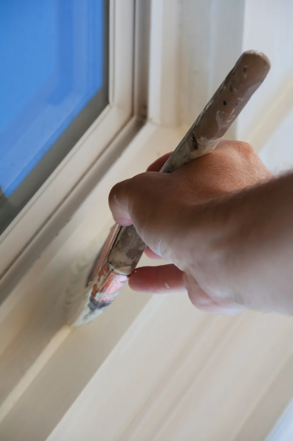 Brush applying white paint to window trim — illustrative craft photography